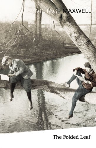 Two young men sit on a fallen tree trunk over water, reading books.
