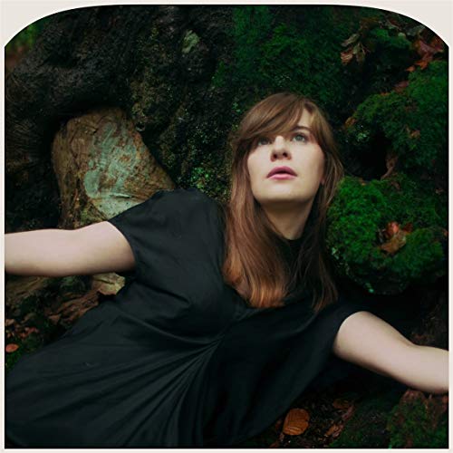 Woman with long brown hair surrounded by lush green moss and trees.