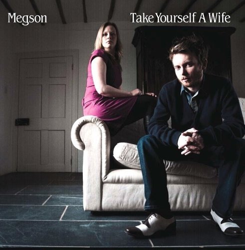 "CD cover with man and woman sitting on a white couch in a dimly lit room."