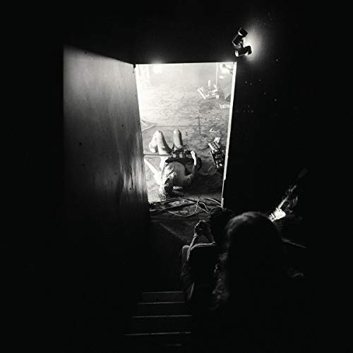 Black and white album cover showing a person lying in a room viewed through a doorway.