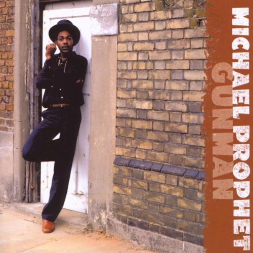 Michael Prophet wearing a hat and black clothes, leaning against a white door frame.