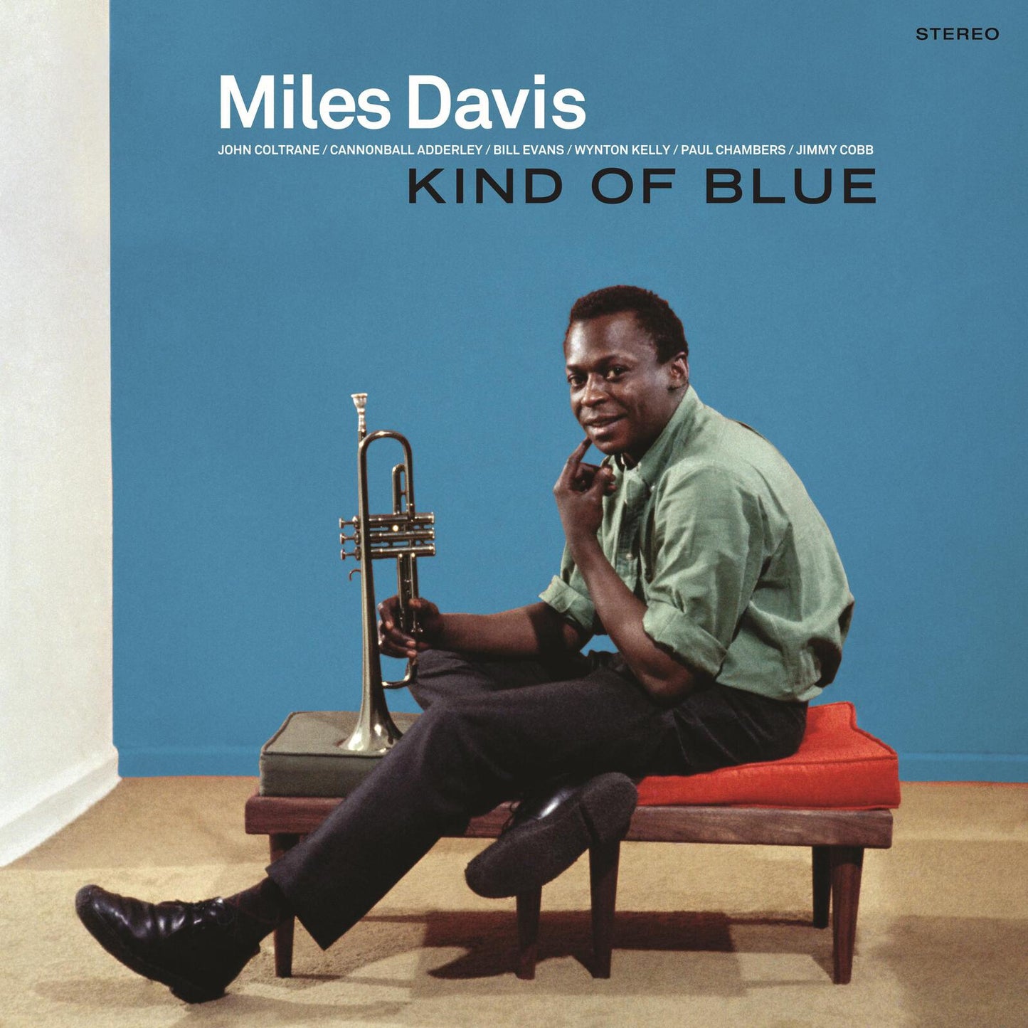 Miles Davis sits on a bench holding a trumpet against a blue background.