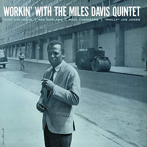 Miles Davis in a suit standing on a city street with a steamroller behind.