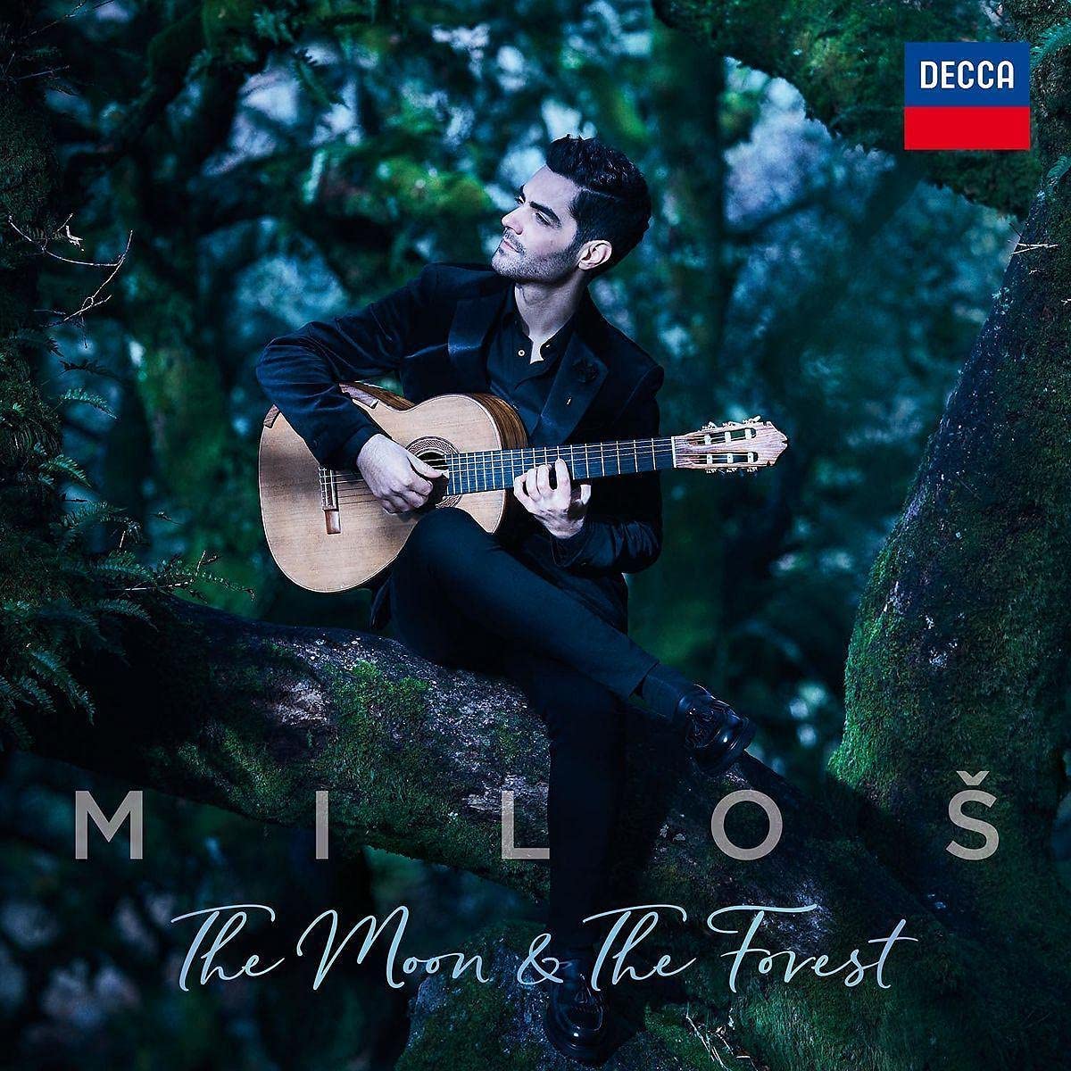 Miloš Karadaglić sits playing a classical guitar in a forest.