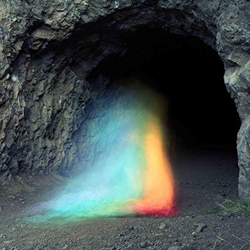 A rainbow-colored mist emerges from the dark opening of a rocky cave.