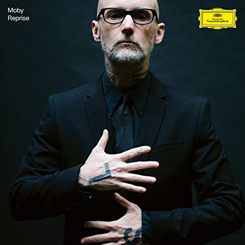 Moby in a black suit, looking at hands with tattoos.