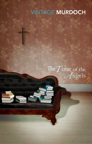 A black Victorian sofa with stacks of books sits before floral wallpaper and a cross.