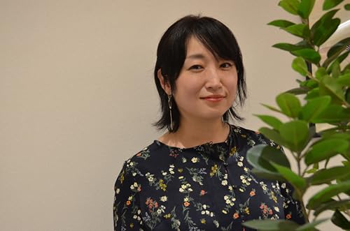 Woman with dark hair and floral shirt, standing near a plant.