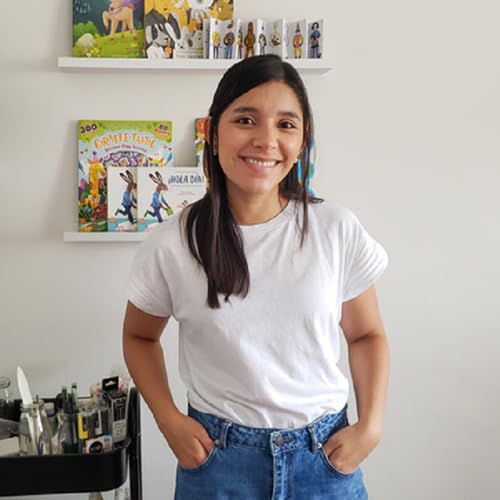 Woman smiling, standing near shelves with children’s books.