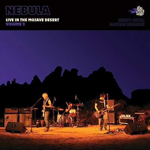 A band performs on a desert stage at twilight with rocky silhouettes in background.