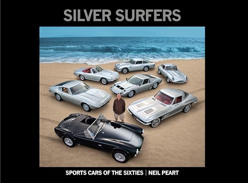 A man standing on a beach surrounded by several vintage silver sports cars.
