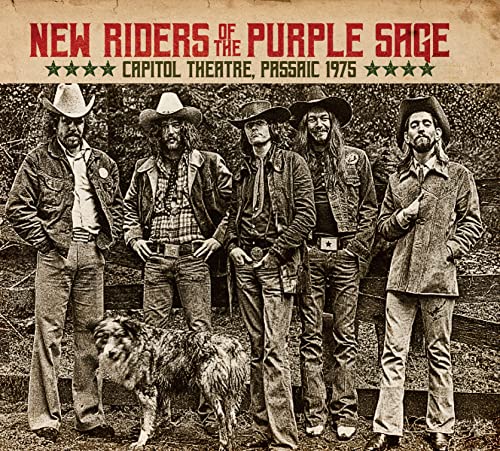 Five men in cowboy hats and a dog stand before a wooden fence.