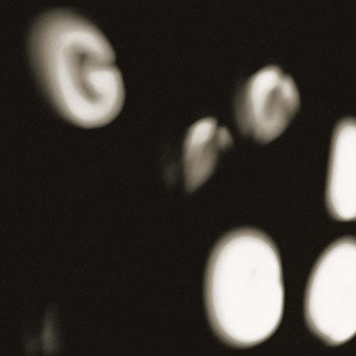 Blurred, close-up image of white shapes resembling letters on a dark background.