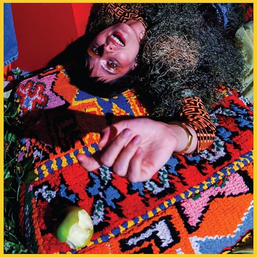 A person with dark curly hair lies on a colorful patterned rug with an apple.