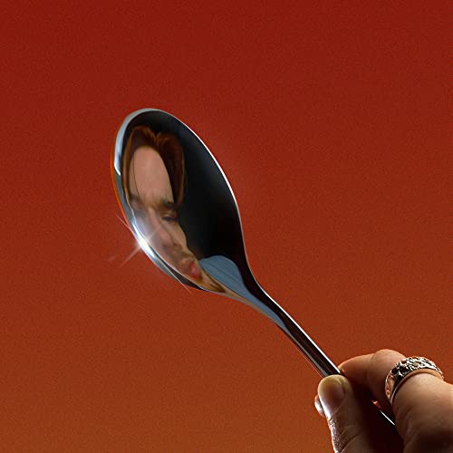 Man’s face reflected in a shiny spoon, held by a hand.