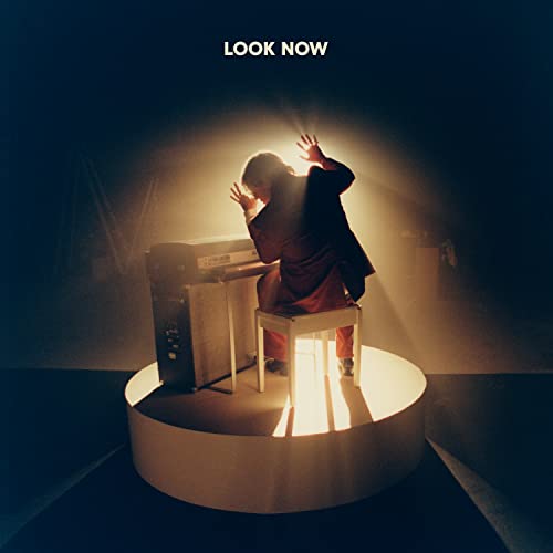 A person in a suit plays a piano on a circular stage under spotlight.