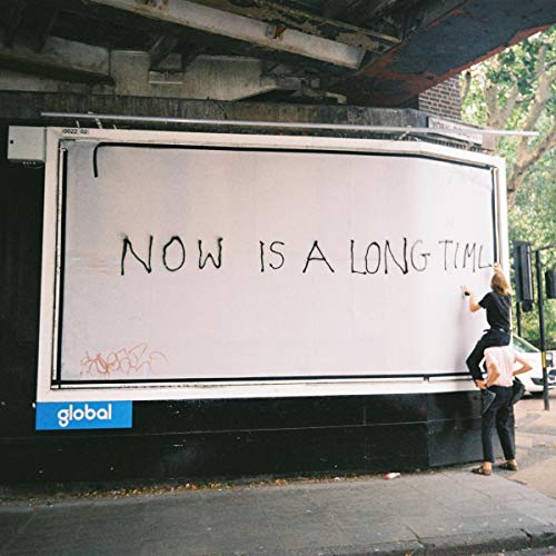 A person standing on another's shoulders writes on a billboard reading Now Is A Long Time.