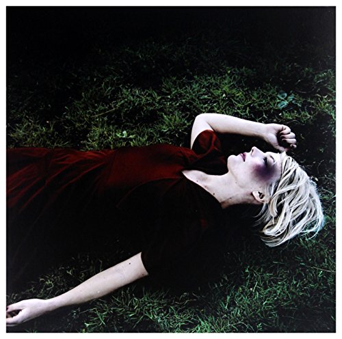 A blonde woman in a dark red dress lies on grass with eyes closed.