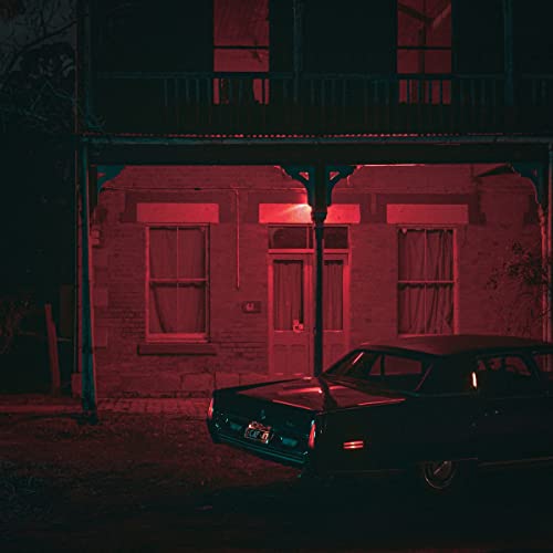 A dark car parked in front of a building illuminated by red light at night.