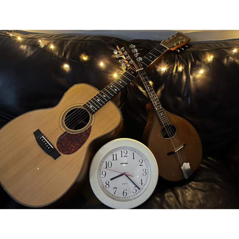 Two acoustic guitars and a white clock on a dark surface.