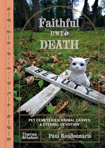 A white cat figurine sits on a wooden cross in a grassy cemetery.