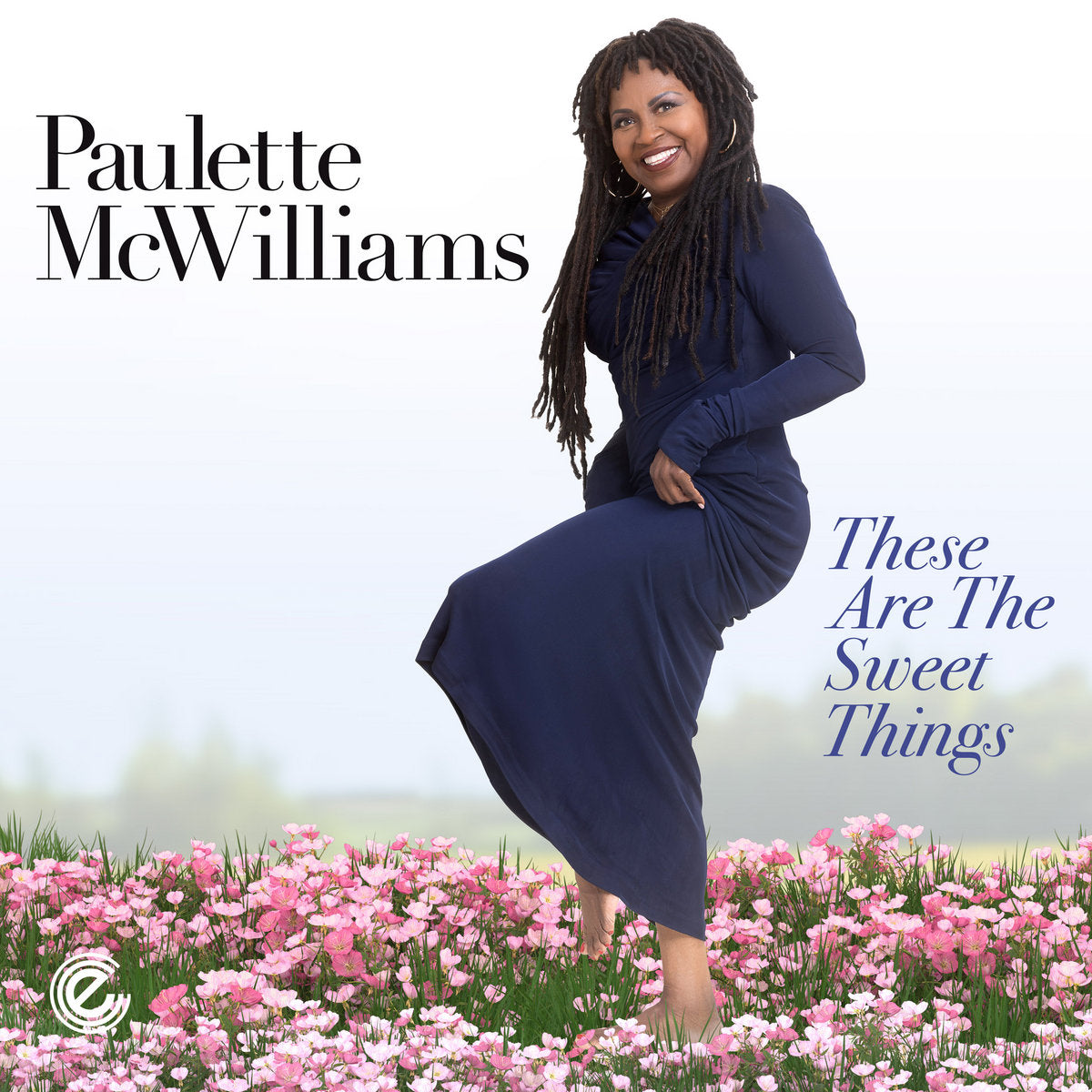 Paulette McWilliams in a blue dress standing in a field of pink flowers.