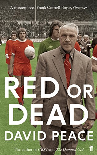 Bill Shankly in a suit stands on a pitch with football players in the background.