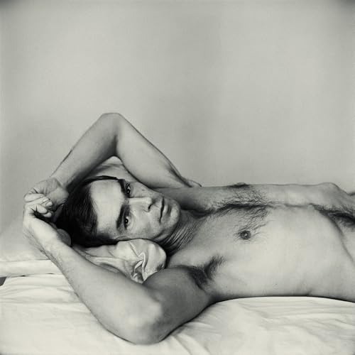Black and white photo of a shirtless man lying on a white bed.