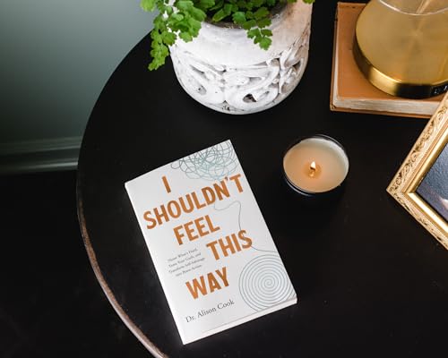 Book cover with orange text, a candle, and a potted plant on a dark table.