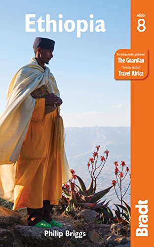 A man in traditional Ethiopian clothing stands on a mountain overlooking a valley.