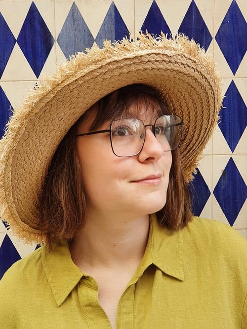 Person wearing a straw hat and glasses, against a blue tile wall.