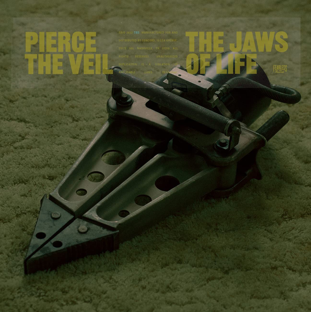 A hydraulic rescue tool sits on a green carpet with band and album text overlay.