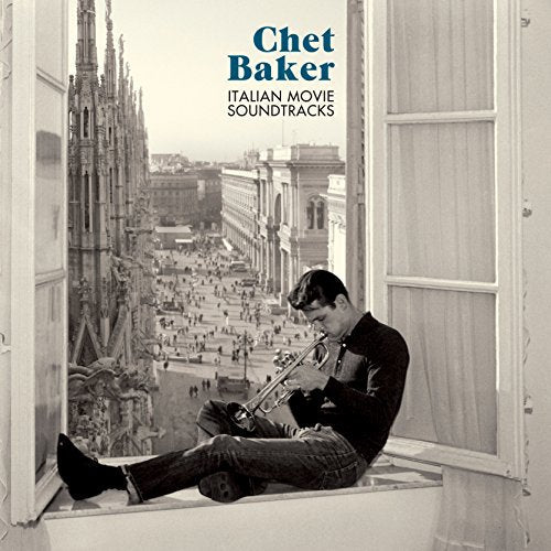 Man sitting on a windowsill playing a trumpet overlooking a city street.