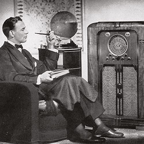 Black and white photo of man sitting with radio and globe behind him.