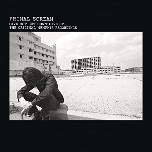Black and white album cover featuring a man crouching in front of buildings.
