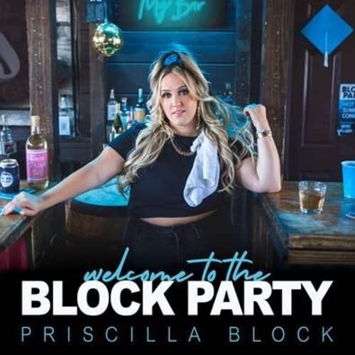 Priscilla Block standing behind a bar with a white cloth tucked into her shirt.