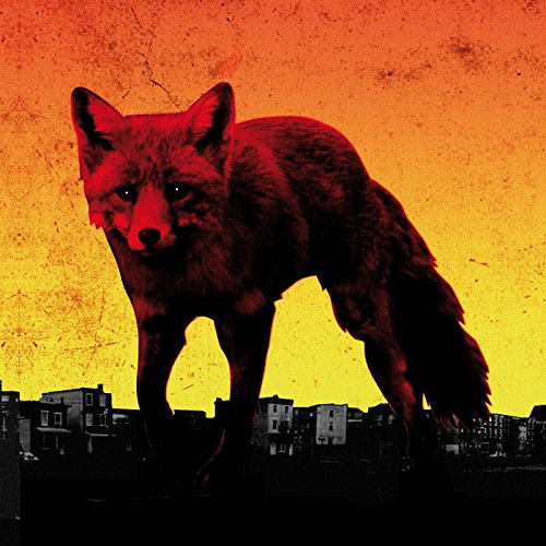 Red fox stands over a silhouetted cityscape against an orange sky.