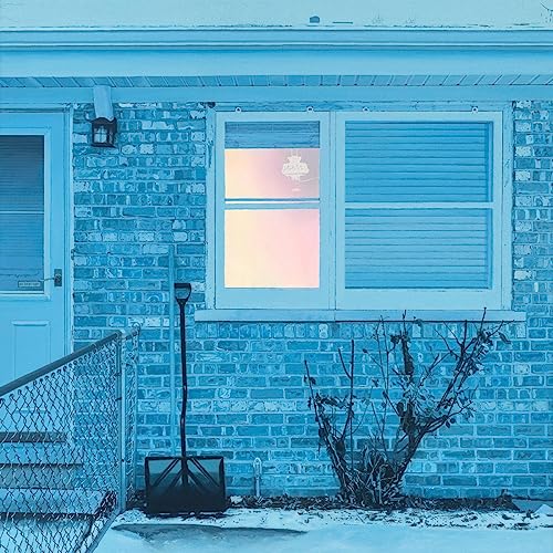 Blue brick house facade with a window and snow-covered ground.