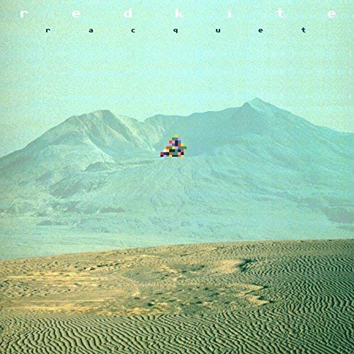 A pixelated, multicolored shape sits on a desert mountain landscape under a pale sky.