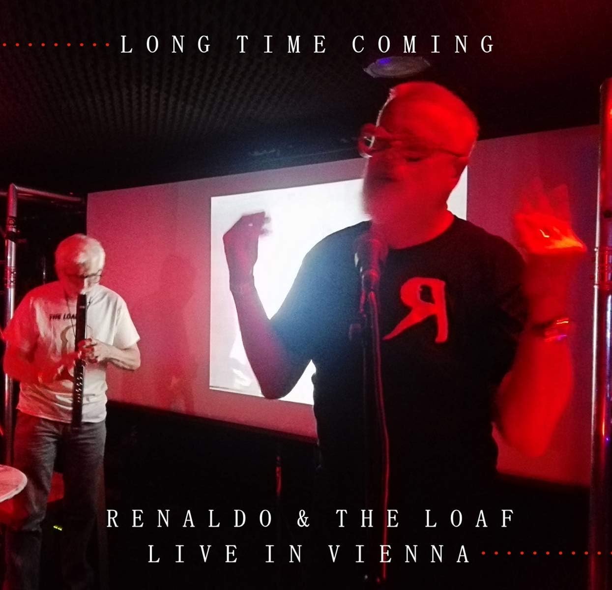 Two men performing on stage under red lighting with text overlays.