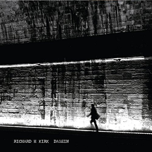 Black and white album cover, a lone figure walking by a concrete wall.