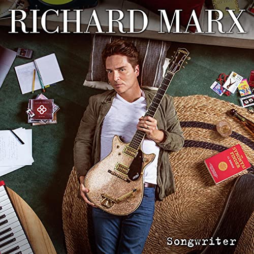 Richard Marx holding a guitar, surrounded by songwriting materials.