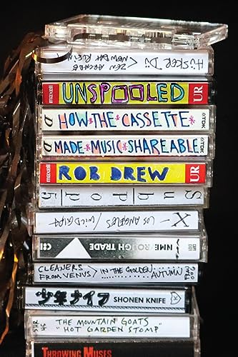 Stack of cassette tapes with handwritten labels and the book "Unspooled" visible.