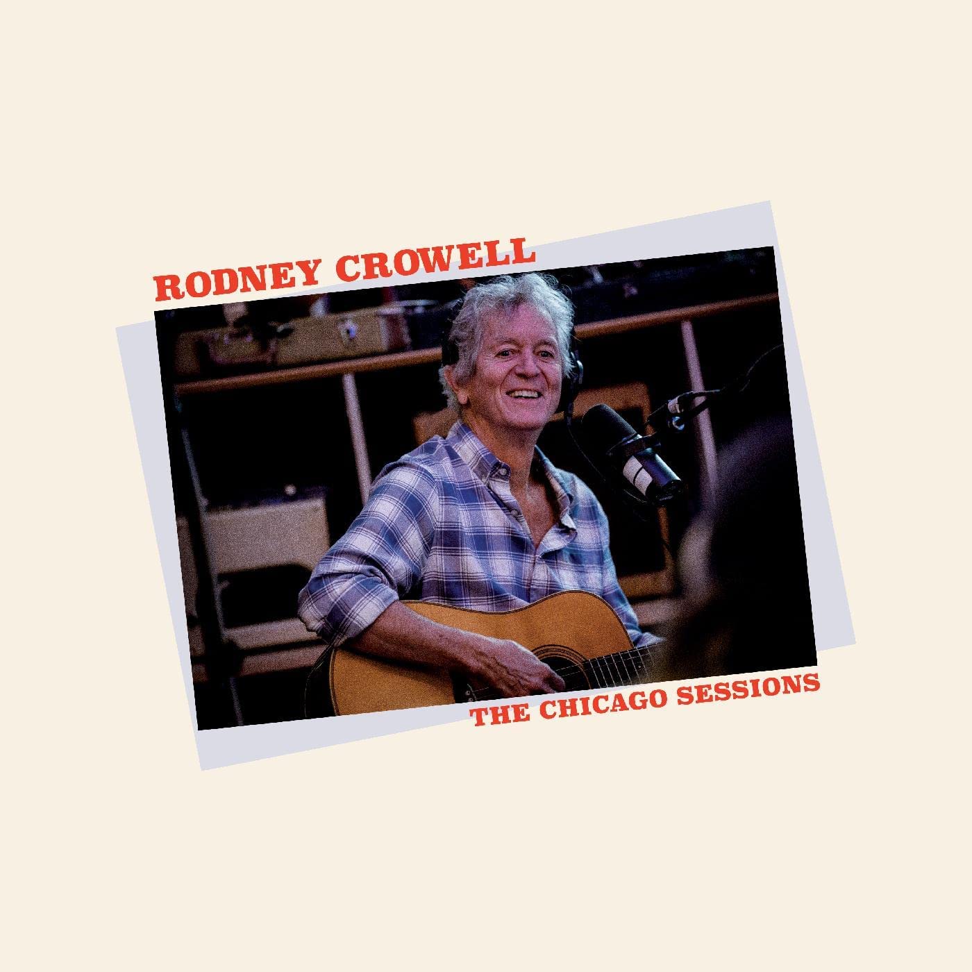 Rodney Crowell smiling with guitar at a microphone in a studio.