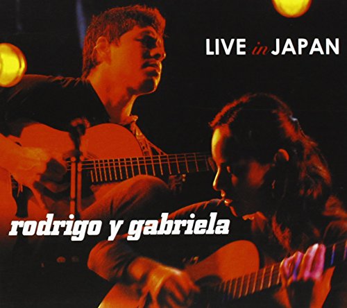 Rodrigo y Gabriela playing acoustic guitars on stage under warm orange stage lighting.