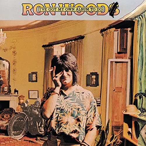 Ron Wood in a floral shirt, holding a cigarette, standing in a yellow room.