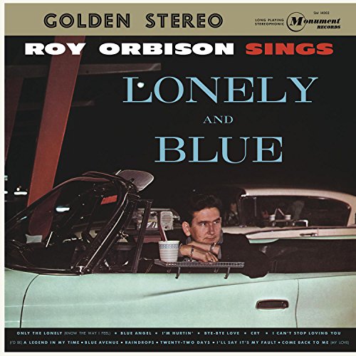 Roy Orbison leans on the door of a light blue convertible car at night.