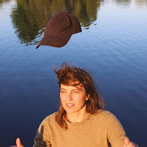 Woman with windswept hair looks up at a floating baseball cap.