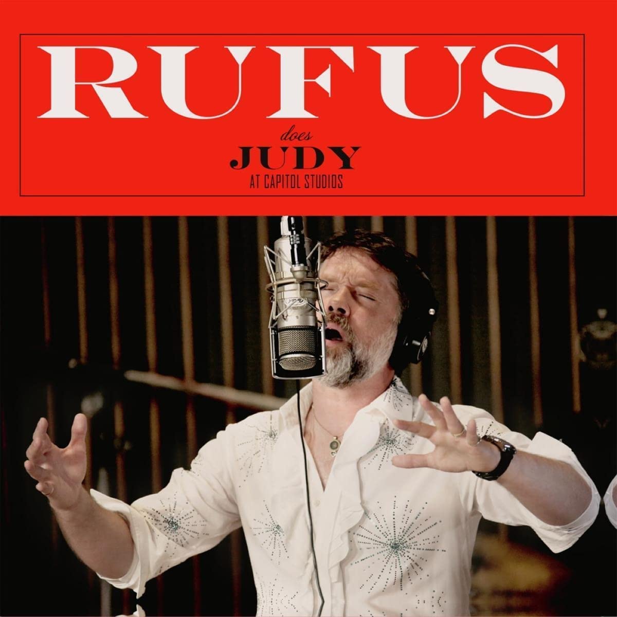 Rufus Wainwright singing into a microphone, wearing headphones, with red title banner above.