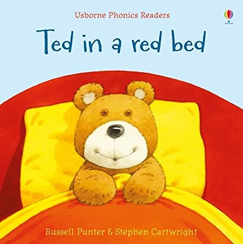 A brown teddy bear sitting in a red bed with a yellow pillow.